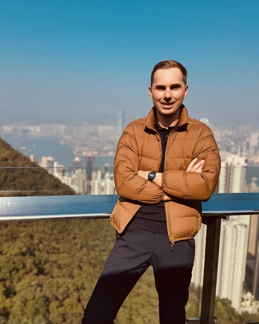 Julien, bras croisés, devant la baie et les gratte-ciel de Hong Kong