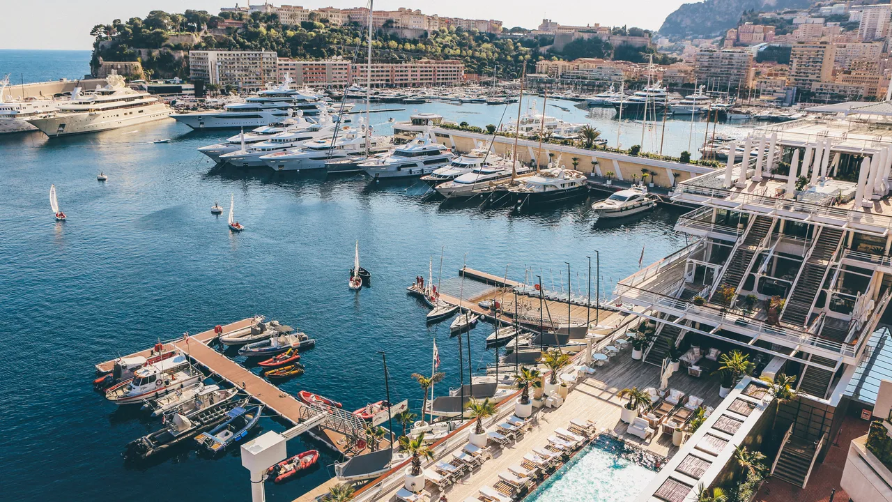 Port Hercule à Monaco vu d'en haut, avec ses yachts amarrés, une piscine en terrasse et la ville à flanc de colline